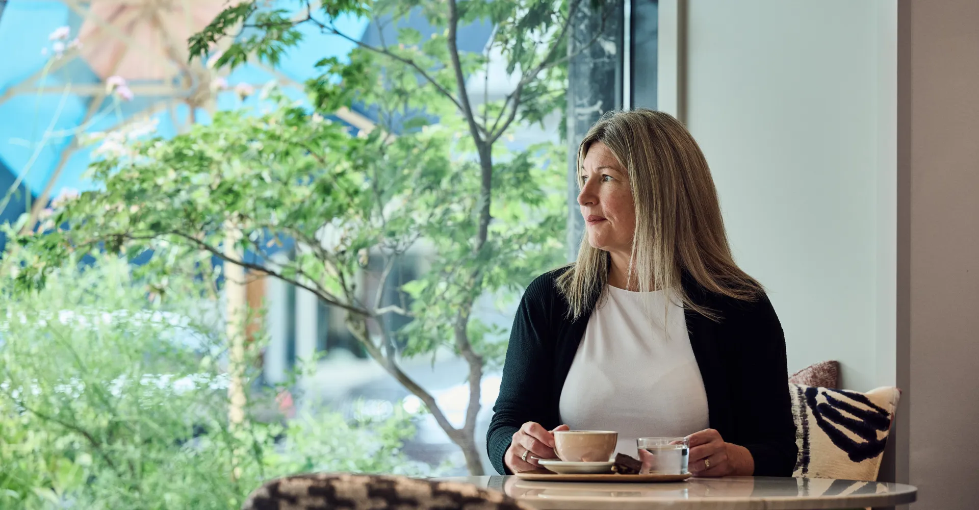 Woman sitting at a table by the window drinking coffee