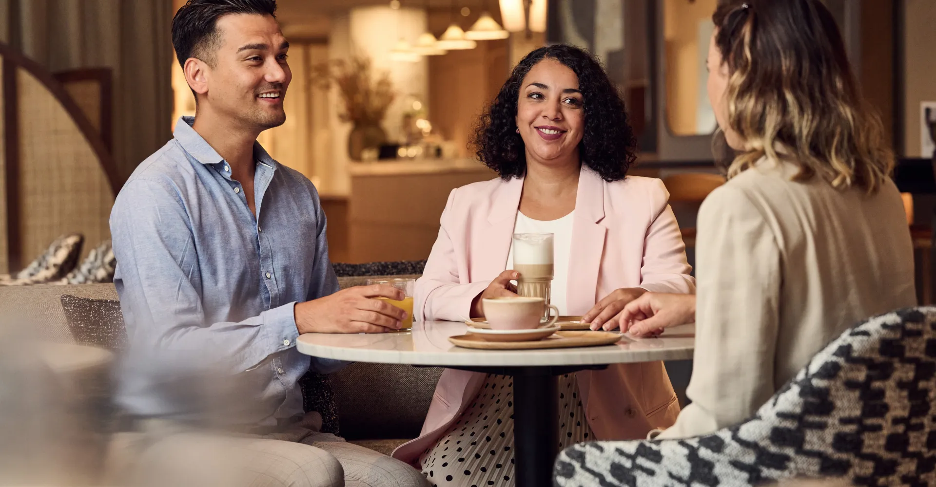 Three people are sitting at a table, drinking coffee and chatting