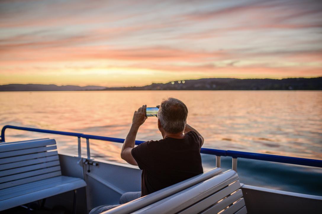 Mann sitz im Schiff auf dem Zürichsee bei Abendstimmung und macht ein Bild