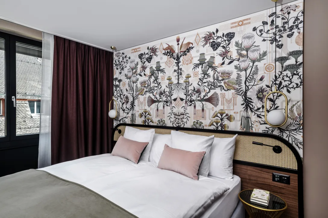 Modernes Hotelzimmer mit Doppelbett, Blumen-Tapete und rosa Kissen.