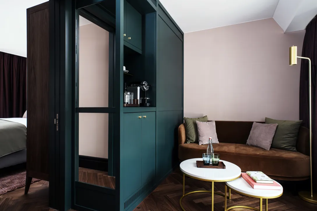 Modernes Hotelzimmer mit Sitzecke, Sofa, kleinen Tischen und Schrank.