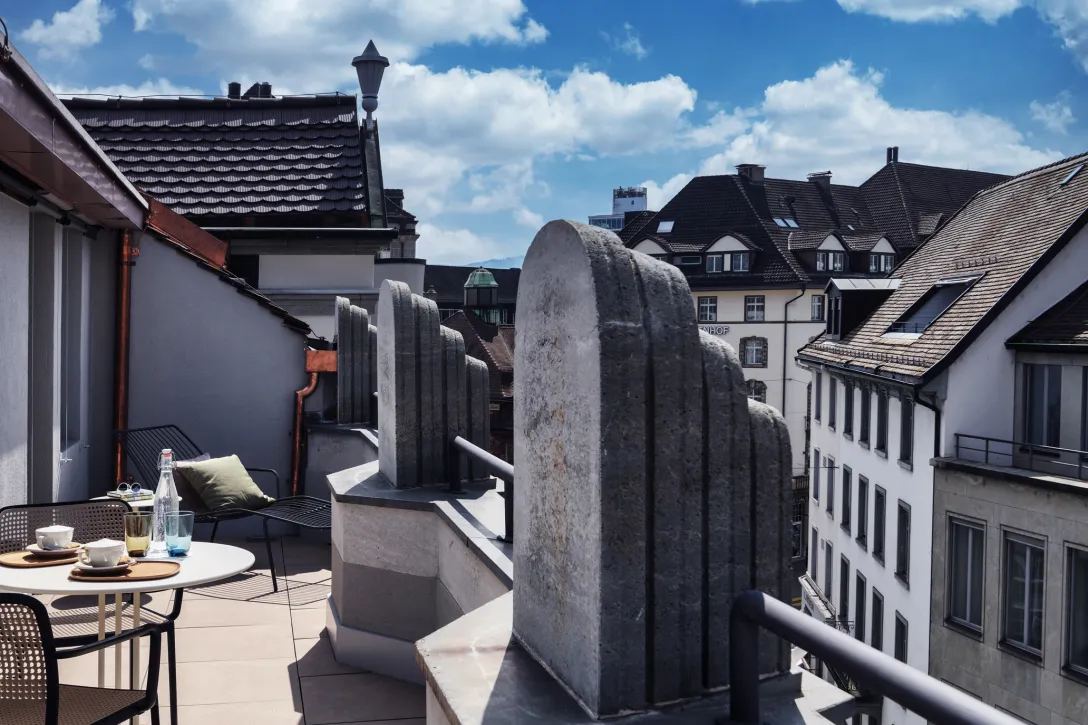 Balkon mit Sitzgelegenheit und Blick auf Dächer der Stadt.