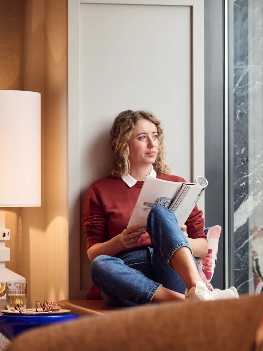 Woman reading a magazine on a windowsill and looking through a window