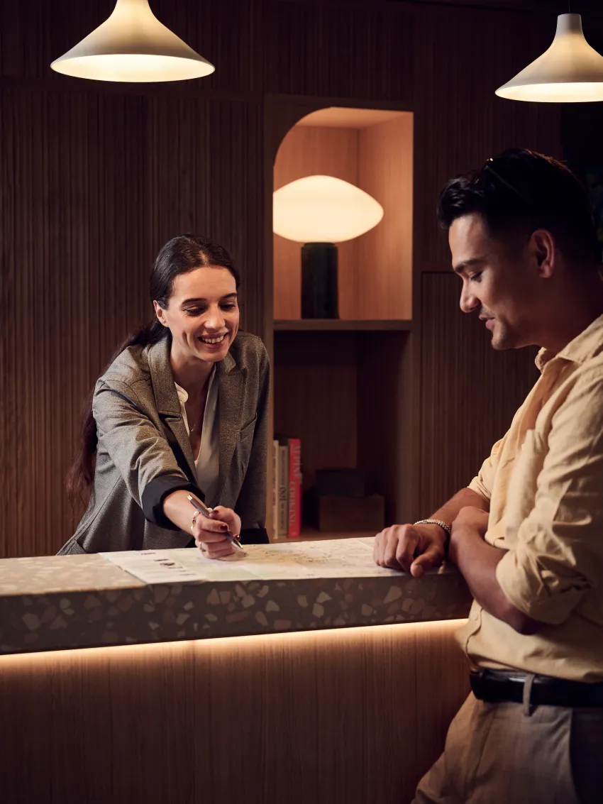 Receptionist explains to a guest how to get to the heart of the action on a city map