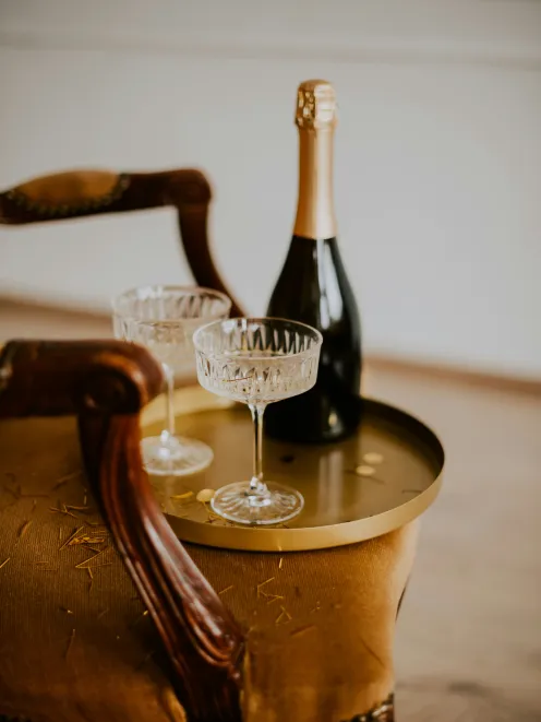A bottle of champagne stands on a wooden table with two glasses
