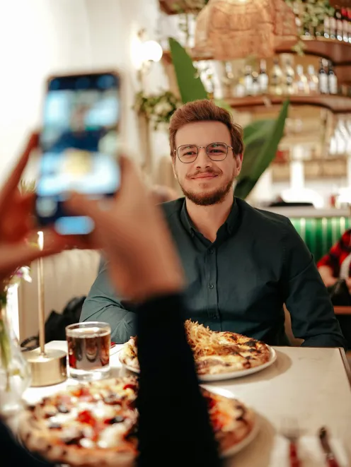 Man sits at the table in front of food and a woman takes a picture of him