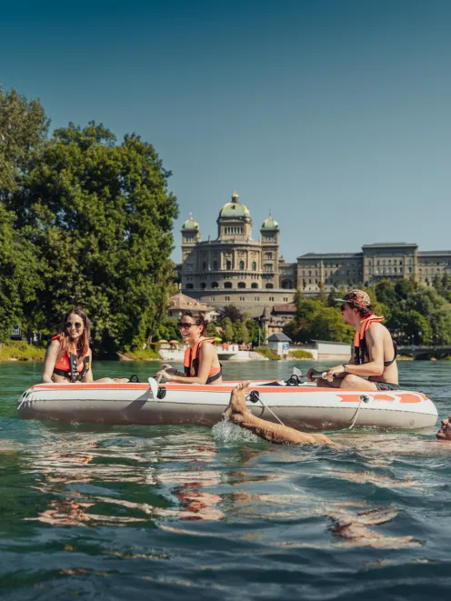People on rubber boats on the Aare in front of the Federal Palace